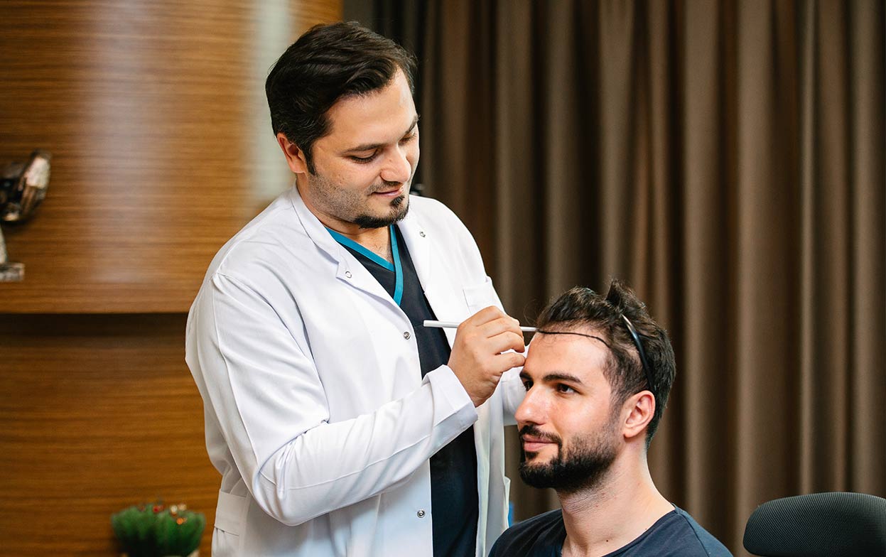 Dr. Balwi a desenhar a linha frontal do cabelo durante a preparação do transplante capilar